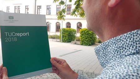 Ein Mann hält ein Exemplar von "TUCreport 2018" in den Händen.