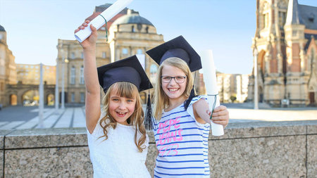 Zwei Kinder mit Doktorhut und Urkunde
