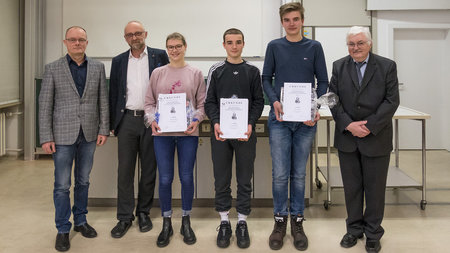 Drei Männer, zwei Schüler und eine Schülerinen stehen vor einer Tafel, die Schüler haben Urkunden in der Hand.