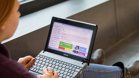 Eine junge Frau hat einen Laptop auf dem Schoß.