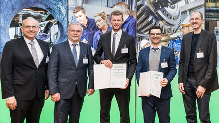 Five men stand side by side in front of a trade fair wall.