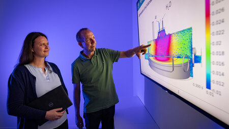 A man and a woman stand side by side and look at a blackboard on which a slide is displayed.