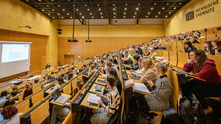 Many people sitting in a lecture hall listening to a professor.