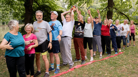Ältere Personen stehen hintereinander auf einem Rasen und geben kopfüber einen Ball von Hand zu Hand.