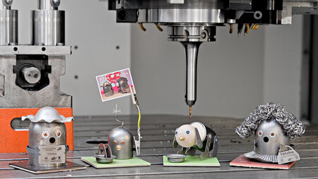 Vier metallische Räucherfiguren stehen nebeneinander im Arbeiitsraum einer Fräsmaschine.