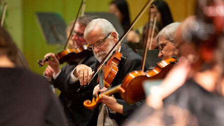 Mann mit Violine sitzt in einem Orchester.